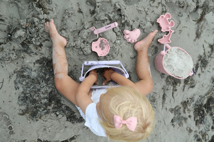 Dziecko siedzi na plaży i bawi się w piasku foremkami