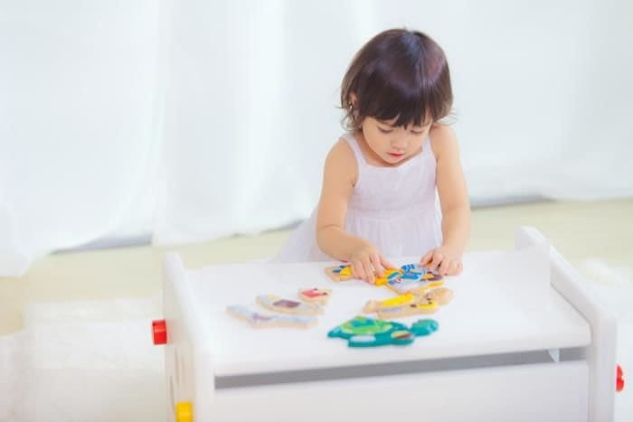 Dziewczynka pochyla się nad stolikiem i układa układankę - puzzle